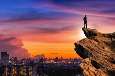 Concept vision, Businessman wearing comfortable casual suit jacket standing chest hug on top of peak mountain and looking forwards with cityscape background, success, competition and leader concept. clipart
