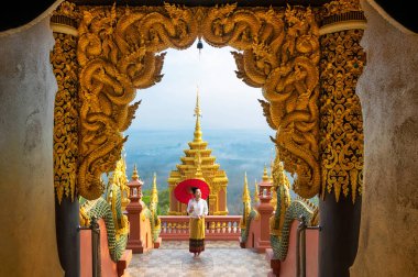 Kuzey giyen Bayan holding kırmızı şemsiye Wat Phra bu DOI Phra Chan Tapınağı, Mae Tha Lampang, Tayland Tayland elbise. (Ortak seyahat ve ibadet için yer)