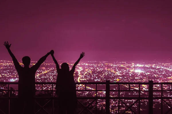 Silhouettes of couple holding hands against night city view