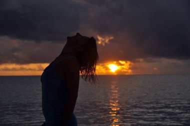 Arka planda gün batımı ile bakarak bir kadının silüeti. Seyşeller