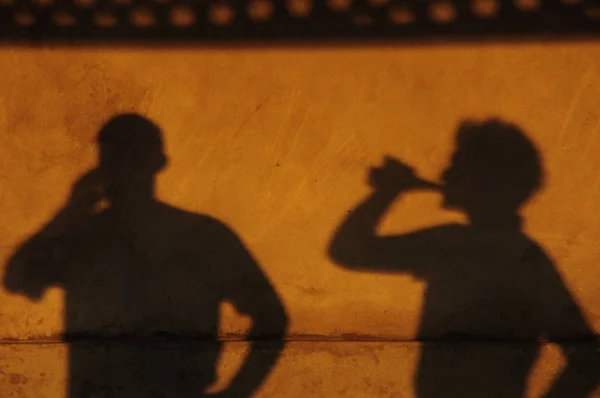 Shadow of people drinking on a yellow wall.