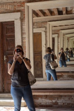 Genç bir kadın aynalarda kendi akıllı telefonuyla fotoğraf çekiyor. Venedik, İtalya