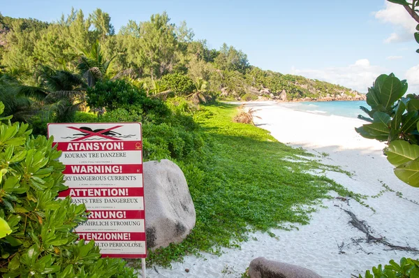 Warning sign post of strong current at the beach of Petite Anse, La Digue island, Seychelles