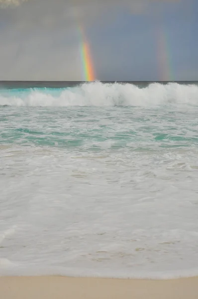 Colourful two rainbows over the sea with waves and sandy beach in Petite Anse, La Digue Island, Indian Ocean, Seychelles