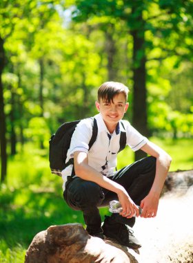 Açık havada yeşil yaz ormandaki bir sırt çantası ile mutlu genç çocuk portresi