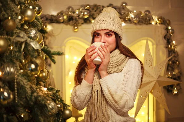 Девушка пьет чашку кофе дома в новогоднем декоре — стоковое фото