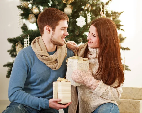 Yeni yıl ağacı arka planda Noel'de evde aşık genç bir aile çift hediyeler vermek
