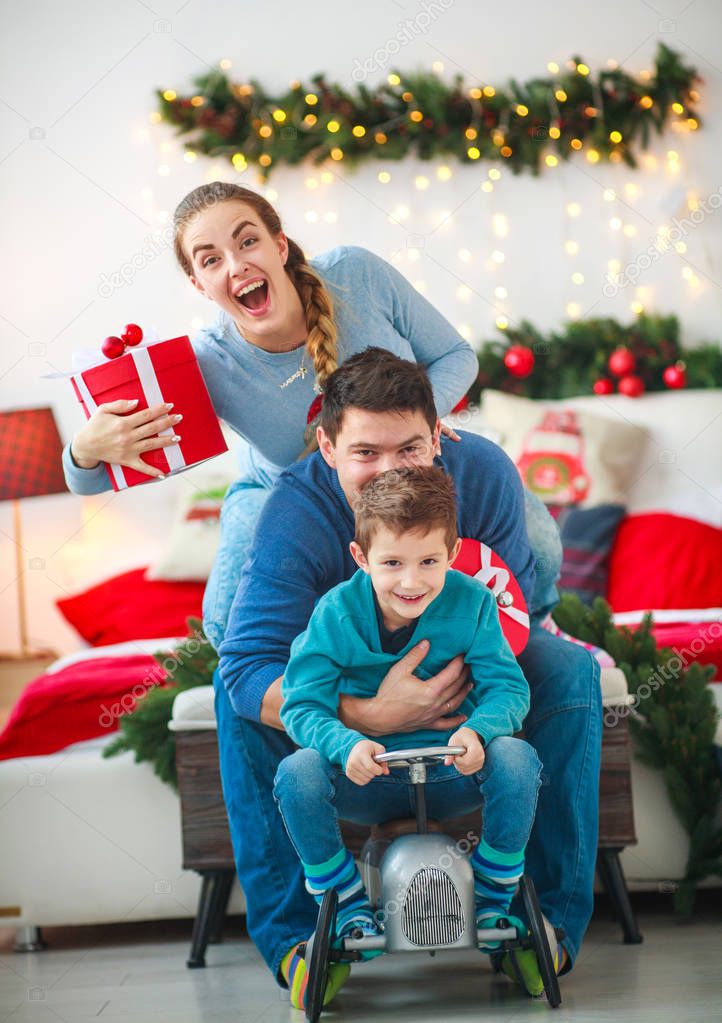 Family couple with a boy with gifts are having fun playing at home in the Christmas decorations
