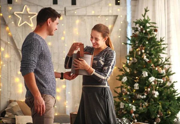 Young joyful couple gives presents at Christmas at home in the New Year\'s interior