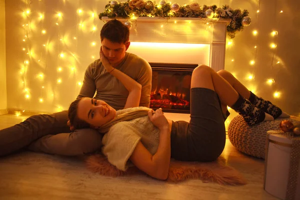 Pasangan muda yang bahagia jatuh cinta di rumah dengan perapian pada hari Natal — Stok Foto