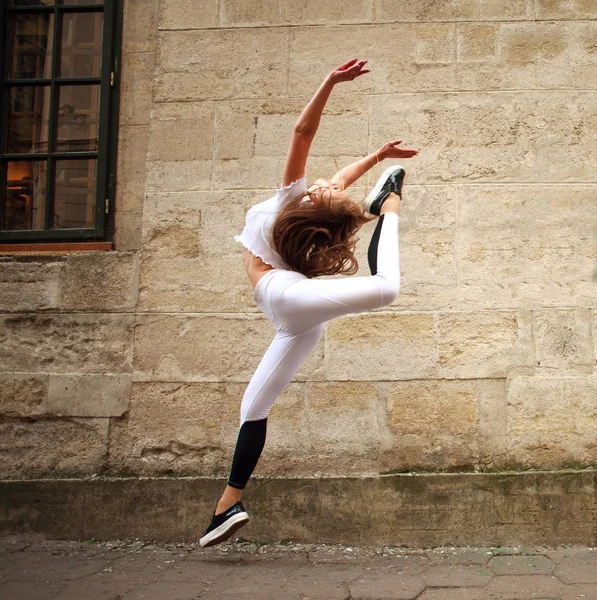 运动运动的女孩在城市街道上做跳跃练习的背景上的老式石墙 — 图库照片