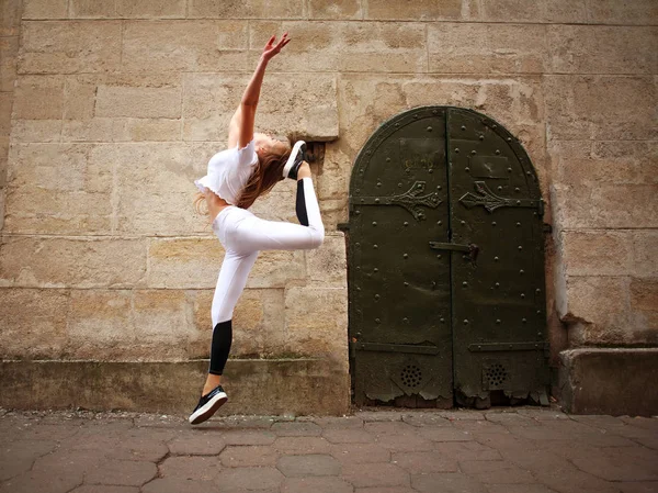 Sport athletic girl doing jumping exercises on the city street on background of vintage stone wall
