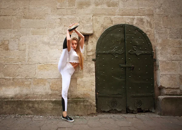 Sport athletic slim girl doing stretching exercises on the city street on background of vintage stone wall