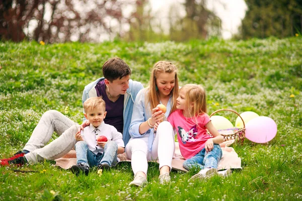Šťastná rodina na pikniku v květnatým parku, kde sedí na trávě, rodič — Stock fotografie