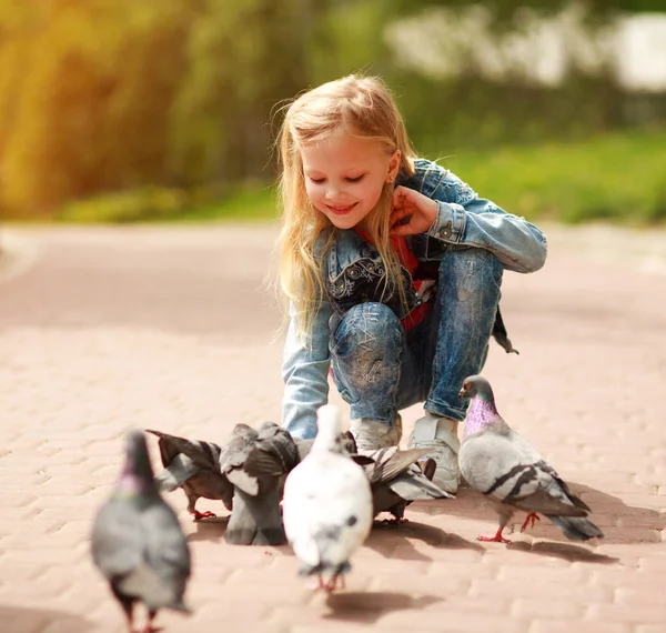 Friendly joyful girl child feeds pigeons in city summer park