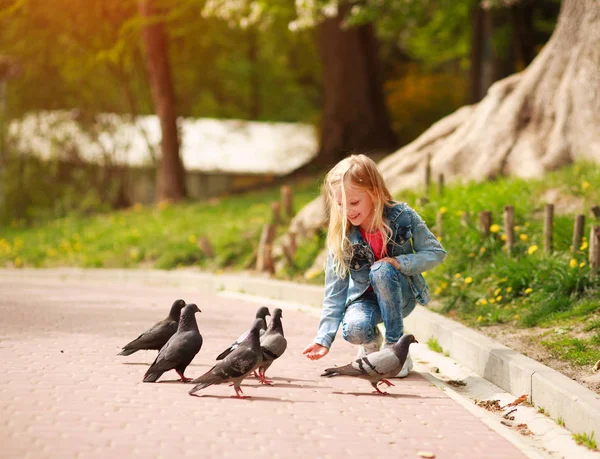 Friendly joyful girl child feeds pigeons in city summer park — Stock Photo, Image