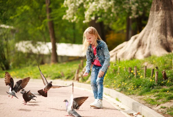 Niña alegre amistosa alimenta a las palomas en el parque de verano de la ciudad — Foto de Stock