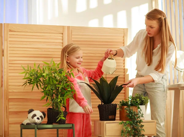 Мать с дочерью поливают зеленые растения в комнате дома Стоковое Изображение