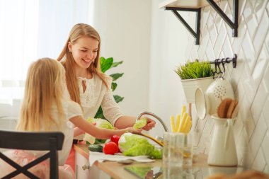 Mutfakta kızı olan mutlu genç bir anne sebzeleri yıkıyor.