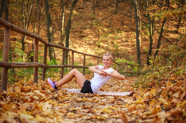 Радостная спортивная девушка занимается фитнес-упражнениями, согревается в лесу — стоковое фото