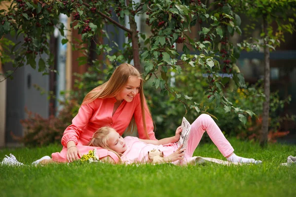 母亲和女儿在自家花园里 一起在城市公园花园里的草坪下的草地上看书 — 图库照片