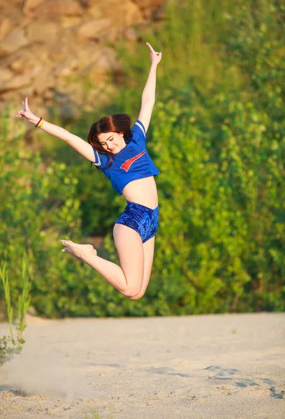 スポーツスレンダーなフィットネスの女の子楽しい緑の木の背景に砂の上にジャンプします — ストック写真