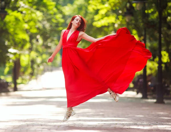 都会の公園でジャンプし 豪華な長い赤いドレスのダンスで若い女性 — ストック写真