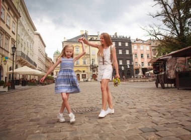 Anne ve kızı, eski turist kasabasının tarihi meydanında neşeyle yürüyorlar.