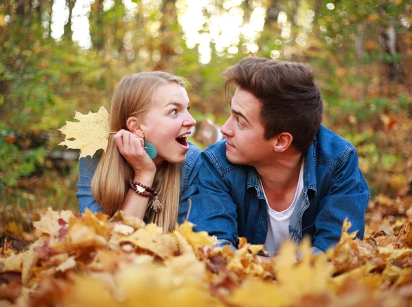 恋のカップル男と女の子は一緒に秋の森の中の落ち葉で楽しんでいます — ストック写真