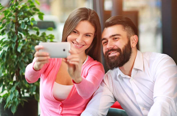 恋爱中快乐的年轻夫妇坐在咖啡店的桌子旁 一边用智能手机自作主张 — 图库照片