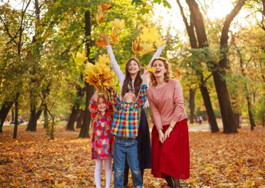 Mutlu ve neşeli bir aile, üç çocuklu bir anne, sonbahar orman parkında sarı yapraklarla birlikte eğleniyor.