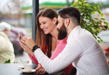 Kafede akıllı telefonlu mutlu ve sevgi dolu bir çift, iletişim kurarken eğleniyorlar.