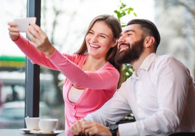 Kafede akıllı telefonlu mutlu ve sevgi dolu bir çift, iletişim kurarken eğleniyorlar.