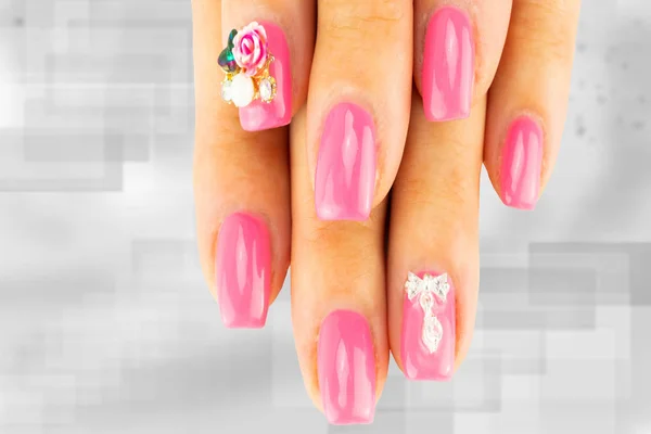 Closeup of beautiful pink nail design at female fingers on bright gray background. Two figure on the nails decorate the pink nail design. Fashion nail design manicure.