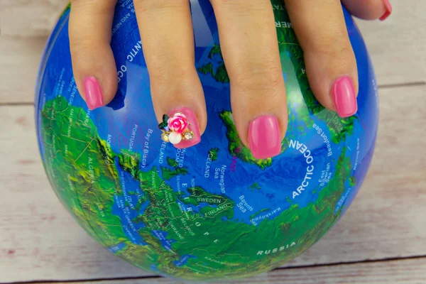 Closeup of beautiful pink nail design at female hand at earth on a wooden table. A figure on the nails decorate the pink nail design. Fashion nail design manicure.