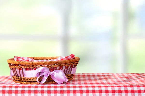 Empty basket with purple ribbon on red checkered tablecloth with bright pastel color background. For your food and product display montage.