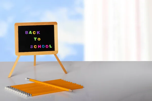 Back to school written with colorful letters on blackboard, and yellow pencils are lying on table in front of bright background. Concept education. Space for your text or display product montage.