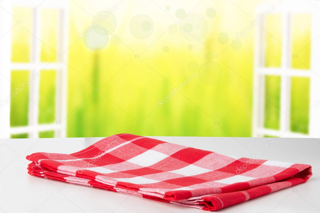 Empty white table top with red checkered napkin or tablecloth on view through a opened window into an abstract light autumn landscape. Space for your food and product display montage.