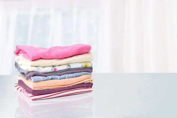 Stack of colorful cute girl clothes. A pile of an colorful clothes on a white table against bright abstract blurred background. Template for your product display montage. Children fashion.
