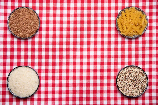 Vegetable food. A frame of four bowls with buckwheat, noodles, rice and quinoa on a red checkered tablecloth. Healthy eating. Top view with space for product montage.