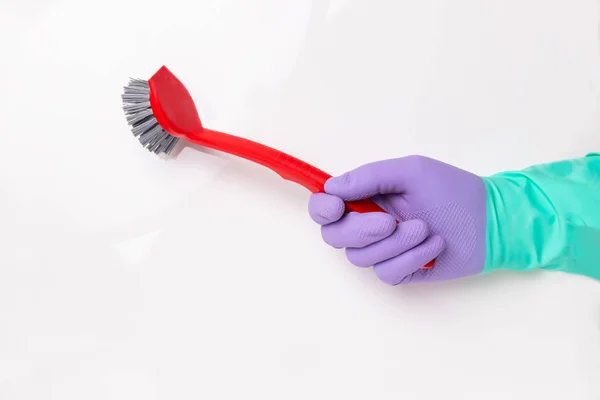 Household glove is holding a red washing-up brush isolated on a white background. Household chore concept.Spring cleaning background. Human hand with a purple and green — Stock Photo, Image