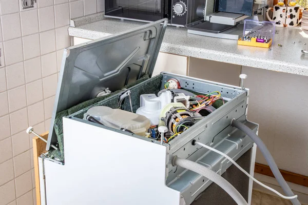People in technician jobs. A broken built-in dishwasher in a white kitchen was removed from the kitchenette then turned upside down and the bottom cover opened.