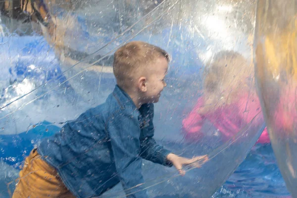 Water or aquac zorbing. Children play inside the inflatabletransparent ball floating in swimming pool. Water walking or zorbing very popular fun activity and suitable for all ages. — Stock Photo, Image