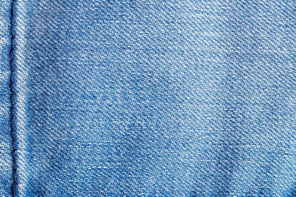 Denim background texture. Close-up of details of empty light blue jeans fabric jean surface with dark blue vertical seam on left side.  Macro. Top view. Beautiful backdrop with space. — Stock Photo, Image