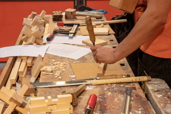 木工车间。一位年轻的男性木工在工作台上用木锤和凿子来工作。锯和螺钉夹是工作场所的进一步专业工具. — 图库照片