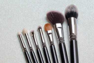 Fotokopi alanı ile ışıldayan parlak arkaplandaki yedi profesyonel makyaj fırçasının yakın çekimi. Kozmetik ürün görüntüleme kurgusu veya reklam metni şablonu. Makro.