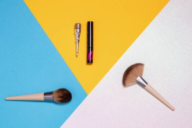 Renkli güzellik ve makyaj ürünleri ve fırça, kaş kalemi, parlak pembe, sarı ve mavi arkaplan üzerindeki ruj gibi araçların dekoratif bileşimi kopya alanı reklam, tasarım, kapak ve kozmetik arka plan..