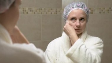 Kadın banyoda ayna önünde pamuk yastık üzerinde yüz bazı tonik ile silinerek