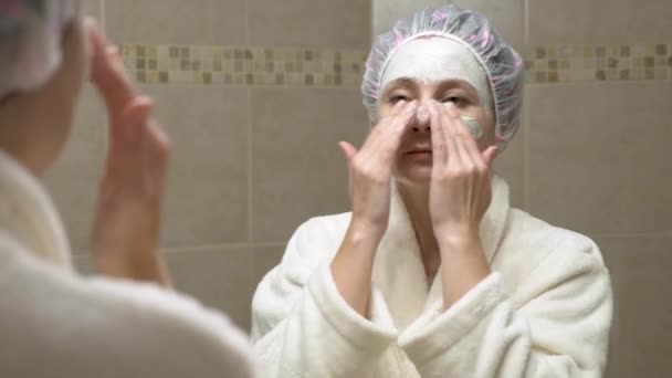 Mujer poniendo mascarilla facial en su cara delante del espejo del baño — Vídeo de stock