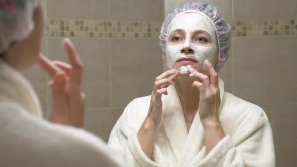 Mujer poniendo mascarilla facial en su cara delante del espejo del baño — Vídeos de Stock